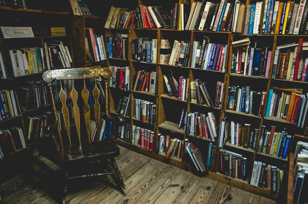 Wide view of a cozy reading nook with a tall bookshelf full of novels